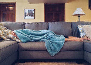 Motivation zum Sport Frau liegt auf der Couch mit Decke über dem Kopf
